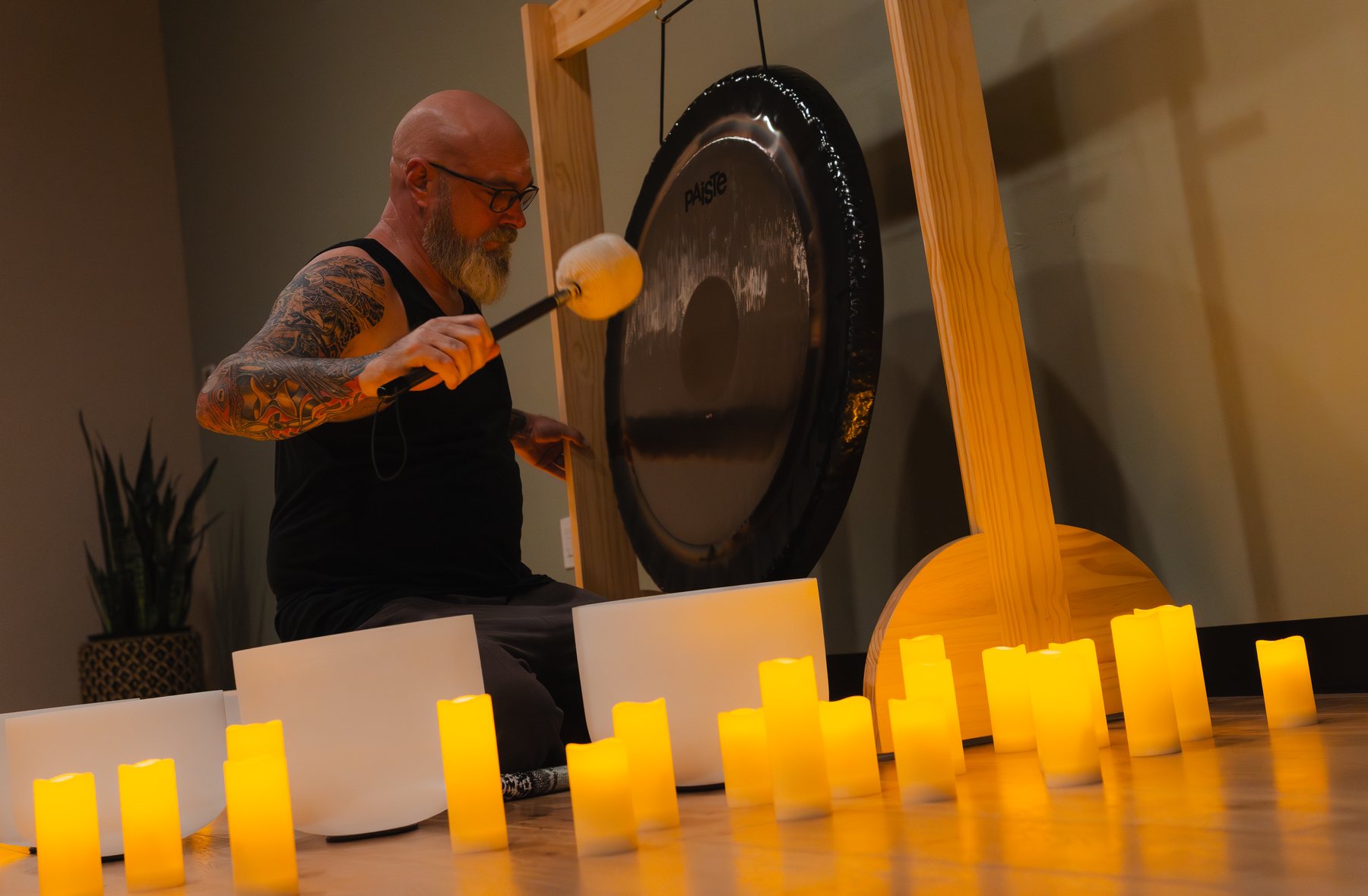 A sound practitioner playing a large gong by candlelight at Gaya's Tree Yoga
