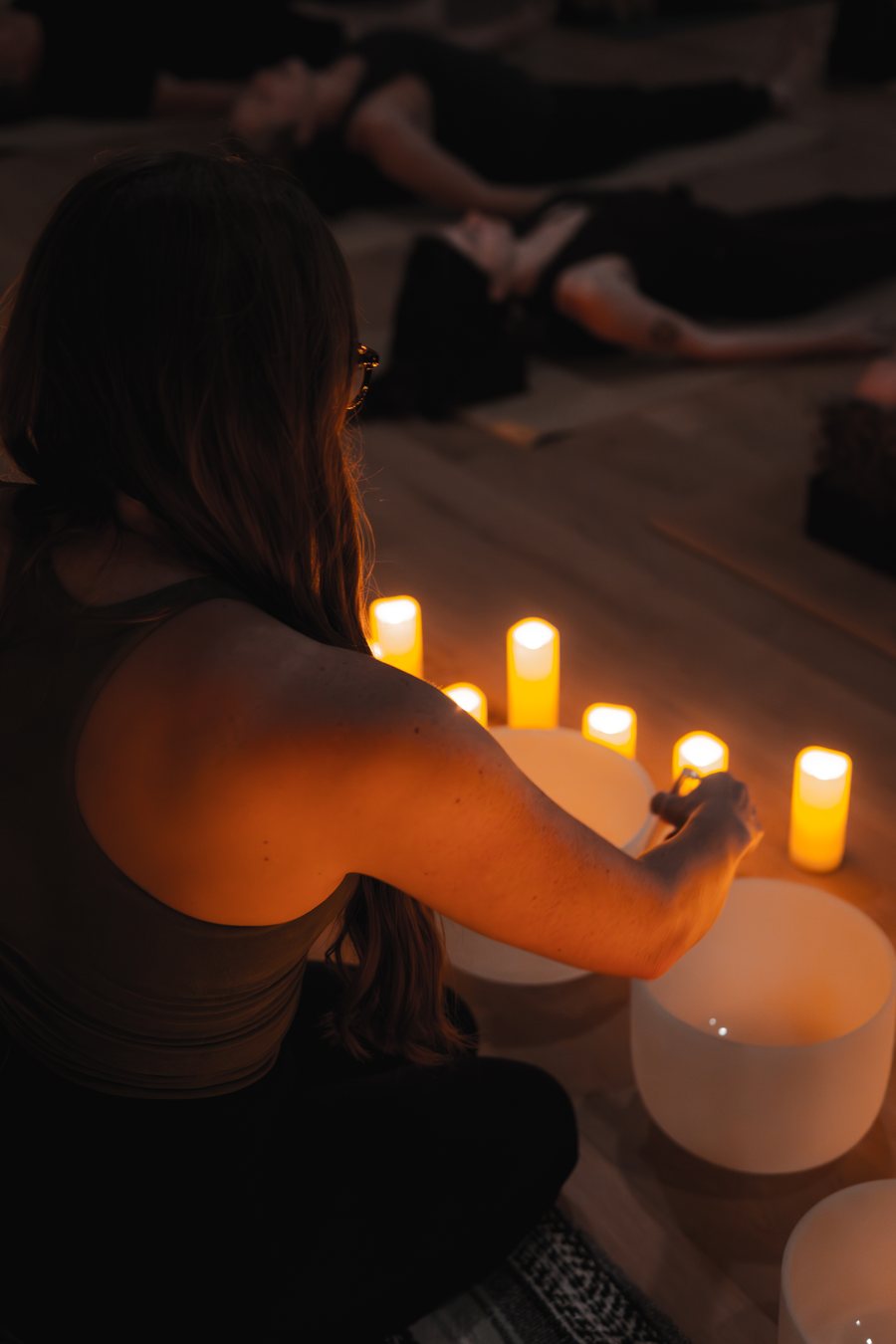 A practitioner holding space with singing bowls while students rest and receive the sound
